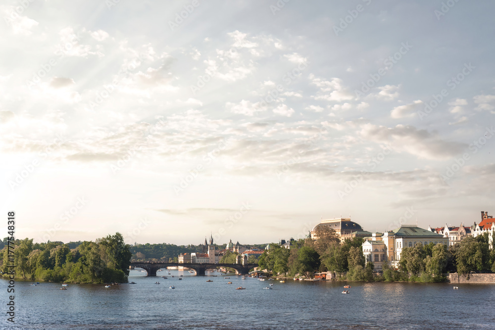 Obraz premium The Vltava river flowing through Prague on a summer day with boats and clouds