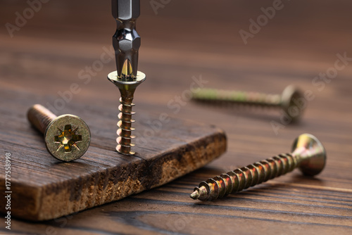 Screwdriver on the screw, screw screwed into timber wood, screw on wooden top table. Close-up, selective focus