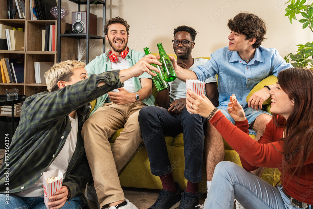 Fototapeta premium Diverse group of friends toasting with beer at home party. Multicultural young people celebrating, concept of friendship, community, and generation z.
