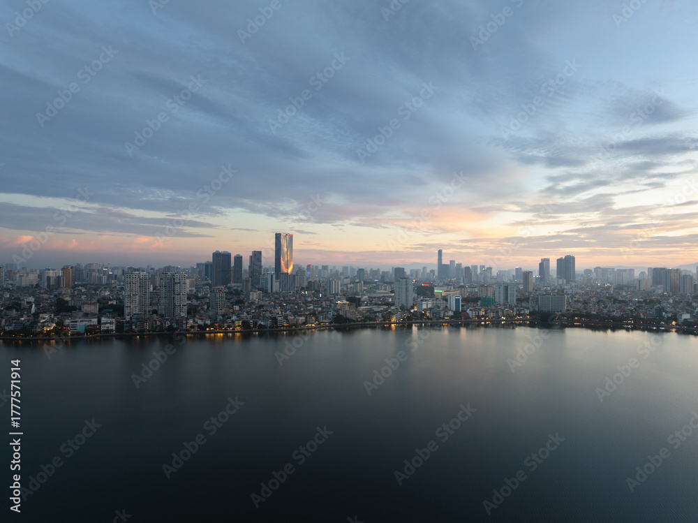 Fototapeta premium Hanoi skyline reflecting on West Lake during early dawn with soft pastel sky and city lights.