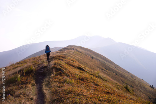 Hiker with backpack walking along scenic mountain trail, autumn landscape, outdoor adventure, trekking in nature
