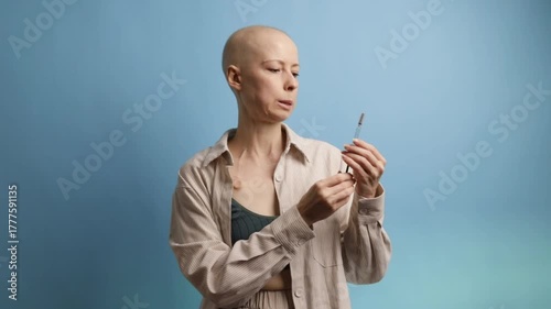 Portrait of woman with cancer in casual clothes holding syringe on blue background, concept of hope, modern medicine, and treatment.