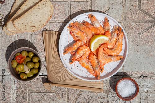 Top view of cooked shrimps on plate and Spanish tapas and elements under hard sunlight