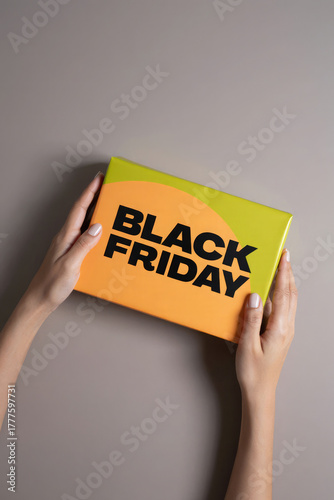 Retail Black Friday promo with hands holding yellow orange gift box, modern bold typography, soft beige background, contemporary holiday shopping visual