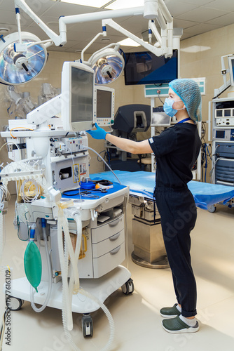 Nurse adjusting equipment monitor in hospital operating room. Medical nurse wearing mask and gloves adjusting monitor settings in surgical room of hospital.