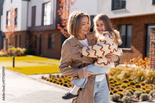 Mother carrying daughter smiling during autumn walk outdoors
