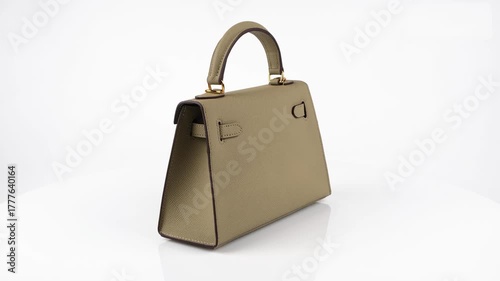 Seamless 360-degree rotation of a stylish light taupe leather handbag with gold clasp and handle. Elegant product video in 4K showcasing luxury fashion accessory isolated on white background.