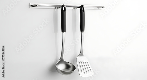 Essential cooking utensils, a stainless steel soup ladle and a slotted spatula, hanging on a modern wall-mounted rack for kitchen organization