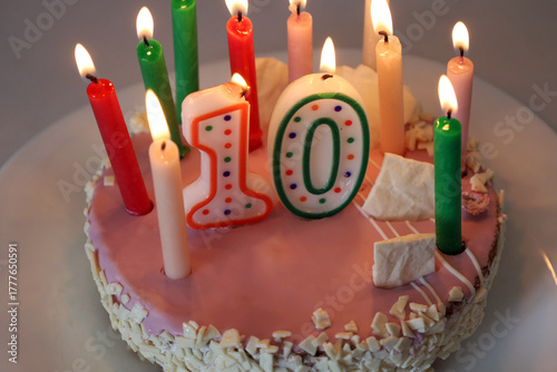 Festive pink and white birthday cake on a light background. Cake for a boy or girl close-up with green, red, pink, white candles and the number ten. Theme of celebrating children's holidays