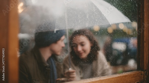 Young couple sitting in front of a window, looking out at each other. the window is covered in raindrops, and the couple is holding an umbrella above their heads.