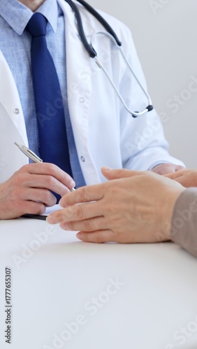 Doctor man taking notes while listening to a female patient explaining her symptoms during a medical consultation in the clinic office. Medicine and health care concept