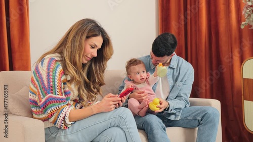 A loving family enjoying precious moments together as they engage with their adorable baby and use their smartphone for entertainment and connection, showcasing the joy of family life.
