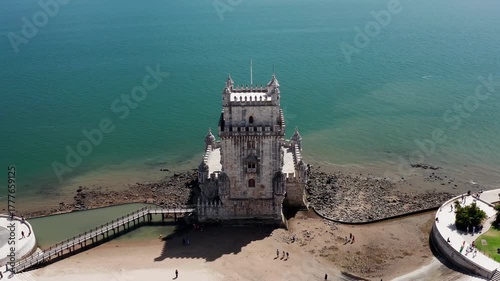 Aerial drone tilt down shot of Belem Tower in Lisbon, a historic fortress on the Tagus River, with tourists visiting and enjoying the iconic monument
