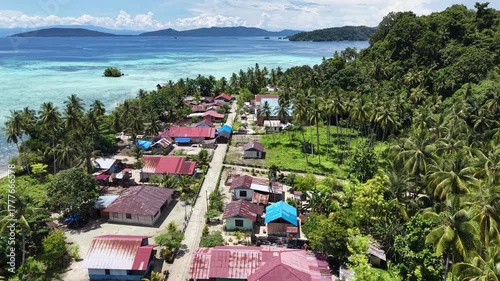 Aerial view of the coastal village on Friwen Island with colorful rooftops, palm trees, and turquoise waters in Raja Ampat, Indonesia.
