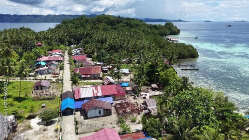 Aerial view of the coastal village on Friwen Island with colorful rooftops, palm trees, and turquoise waters in Raja Ampat, Indonesia.
