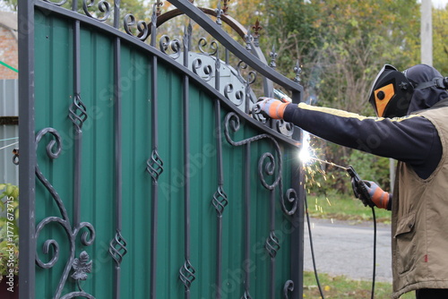 A man repairs a gate at home using a welding machine.