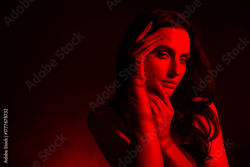 Sensual tender young woman with brunette curls and glowing red light in a stylish artistic photoshoot