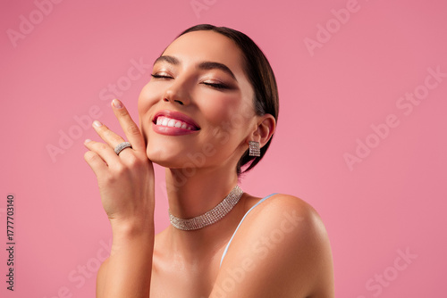 Beautiful young woman with stunning jewelry and glamorous makeup posing against a soft pink background