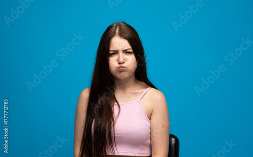 Εκτύπωση καμβά Playful brunette woman with long hair puffing cheeks making funny face blue back