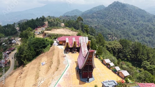 Aerial view of traditional Tongkonan houses with curved roofs on a hillside in Tana Toraja, Indonesia, surrounded by mountains and clouds.	
