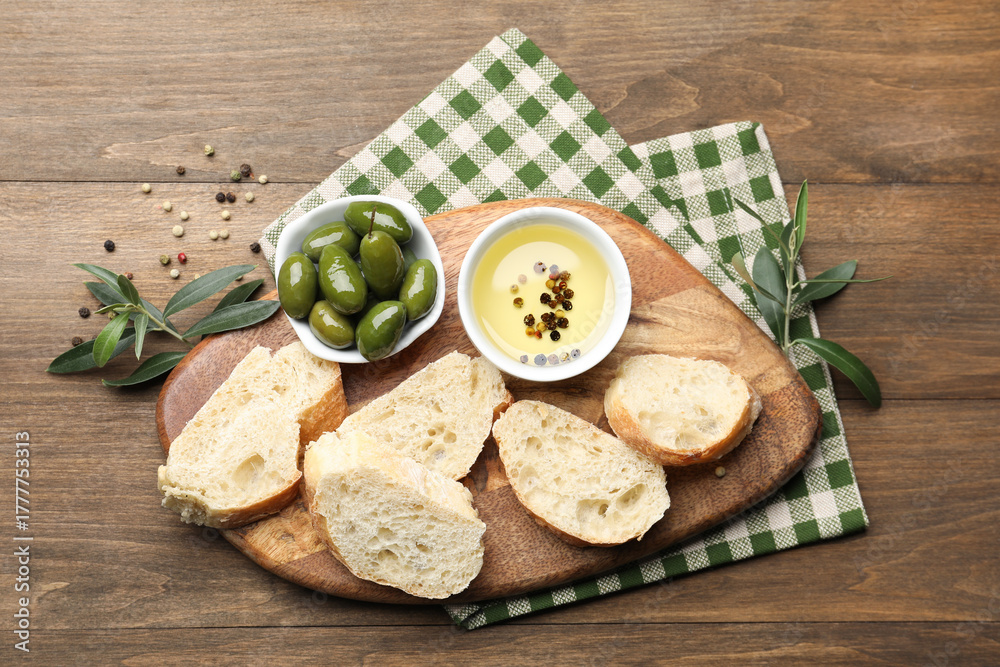 Fototapeta premium Ciabatta slices, oil with peppercorns and olives on wooden table, flat lay