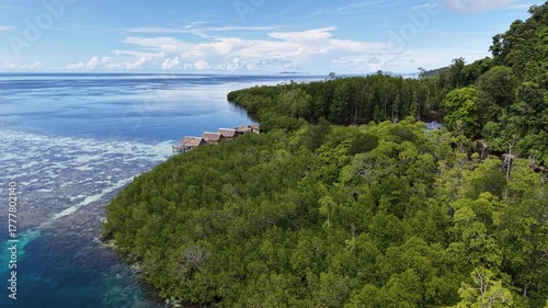 Aerial view of a vibrant blue lagoon surrounded by coral reefs and dense coastal jungle in Raja Ampat, Indonesia.	