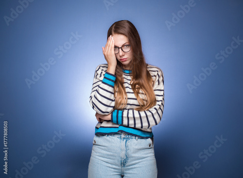 Ashamed woman covering face with hand. Shame, isolated on blue background. Guilty girl.