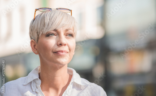 Beautiful middle aged woman with blond short hair wearing sunglasses. Profile of female person dressed in white summer shirt. Outdoors-outside