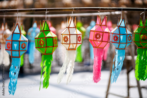 Colorful traditional Lanna paper lanterns (Yee Peng) hanging on a bamboo pole. Focus is on the vibrant Thai northern culture and decoration.