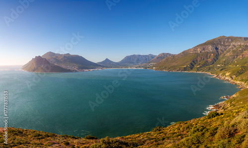 Stunning panoramic view of Hout Bay and coastal mountains from Chapman’s Peak view point, Cape Town, Western Cape, South Africa. A blue bay, rugged peaks, South African scenery beneath a blue sky.