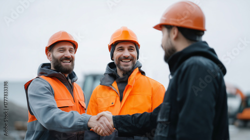 Three construction workers outdoors on a cloudy day, wearing protective helmets, safety vests, and work uniforms, shaking hands and smiling after a successful project discussion. T