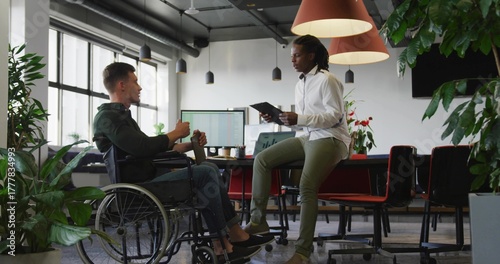 Discussing two colleagues wearing business casual sharing ideas in office, with wheelchair tablet