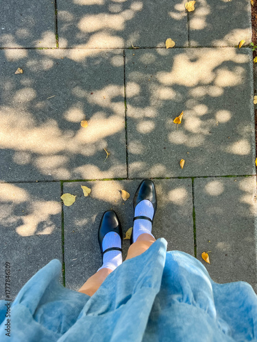 Point of view shot of person wearing light blue jeans and white sneakers walking on patterned pavement in Warsaw Poland city. High quality photograph.