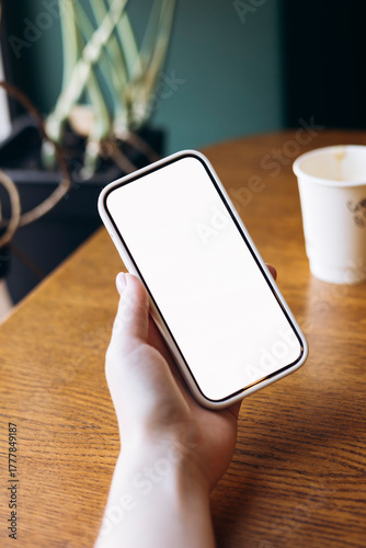 Woman holding smartphone with blank screen and coffee cup.