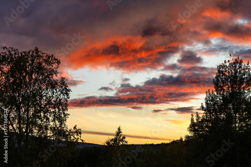 Magical sunset vibrant red orange clouds above a dark trees silhouettes in Sweden