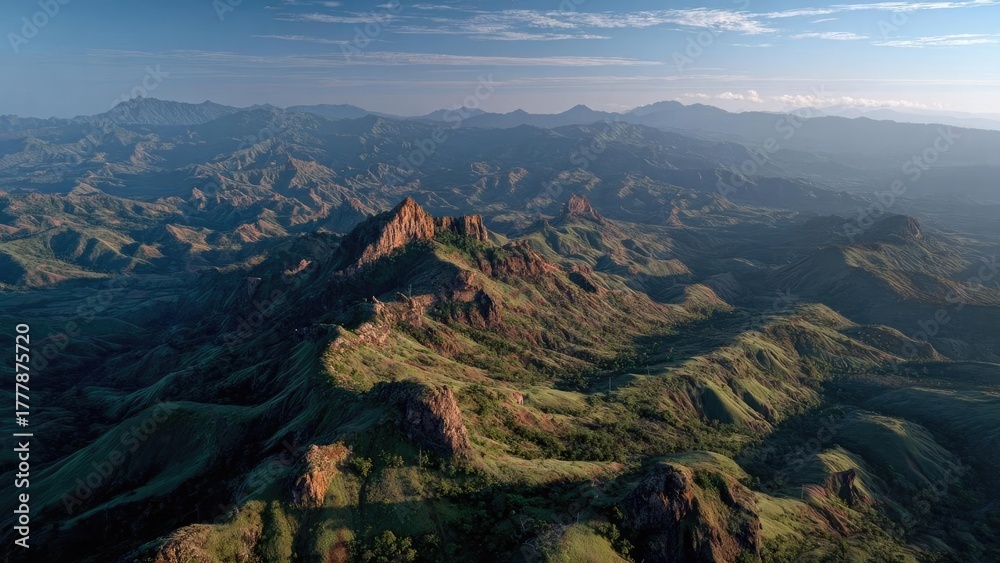 Fototapeta premium A vast green mountain landscape with rugged rocky peaks, rolling ridges and distant valleys under a clear blue sky. Concept Mountain Landscape, Rugged Peaks, Rolling Ridges, Distant Valleys