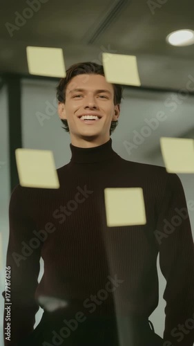 A man in a brown sweater stands in front of a wall covered in yellow sticky notes. Concept of creativity and brainstorming, as the man is in the middle of a meeting or discussion