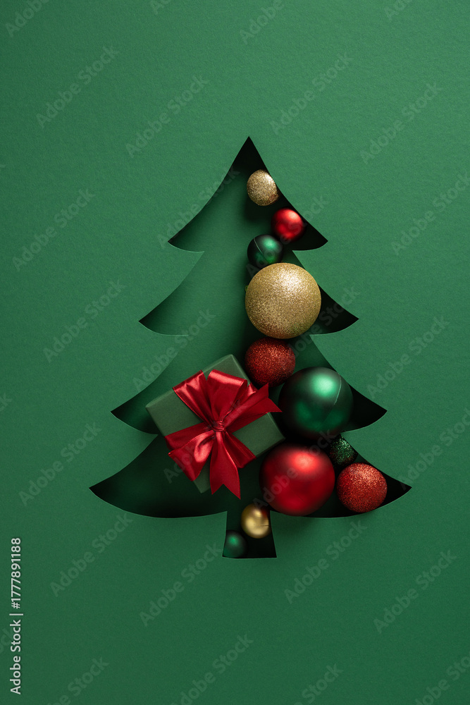 Fototapeta premium Elegant cutout Christmas tree reveals colorful ornaments and a red ribbon gift, set against a deep green backdrop. Ideal for holiday cards, seasonal promotions, and festive greetings