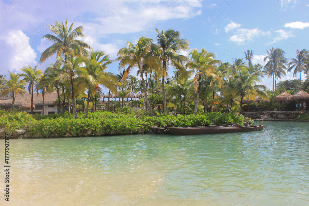Obraz premium Tropical lagoon with palm trees and wooden boats under blue sky, calm paradise in Mexico