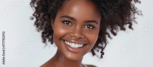 Charming young woman with natural curly hair smiling joyfully in a bright studio, representing confidence, self-love, and modern beauty.