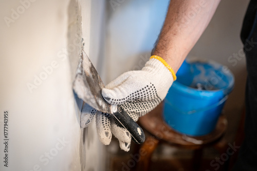 Close-up of a worker's gloved hand using a small putty knife to press thick patching compound firmly into a hole in the interior wall.