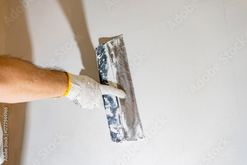 Принти на полотні Gloved worker actively spreads white spackling compound with a finishing tool, preparing the textured wall for a final coat