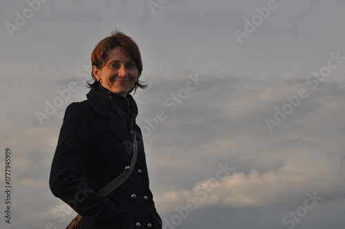 Woman stands confidently outdoors against a cloudy sky during sunset, showcasing a serene and reflective moment
