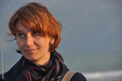 Woman with short red hair enjoys a breezy day by the sea with soft waves in the background