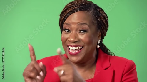 A vibrant and expressive African American woman in a red blazer smiles and points with enthusiasm against a bright green screen conveying excitement and direction.