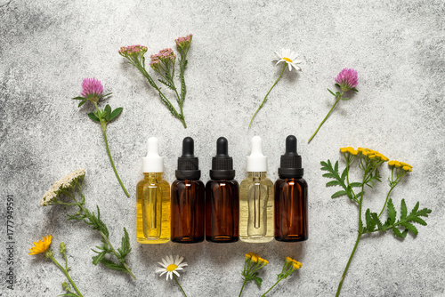 Set glass dropper bottles with essential oil or serum on grunge background with wild flowers, natural cosmetic products, top view, flat lay