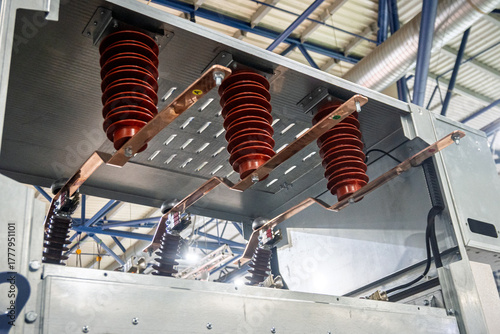 Photos Close-up of high-voltage electrical switchgear components, featuring robust red insulators and shiny copper busbars within an industrial power distribution system