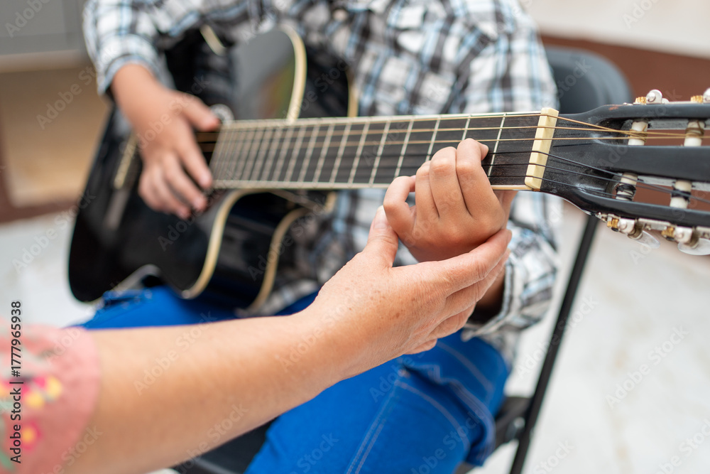 Fototapeta premium Close-up of teacher’s hand adjusting a young student’s hand on the acoustic guitar, showing correct playing position and technique. Music education, learning instrument, teaching guidance concept