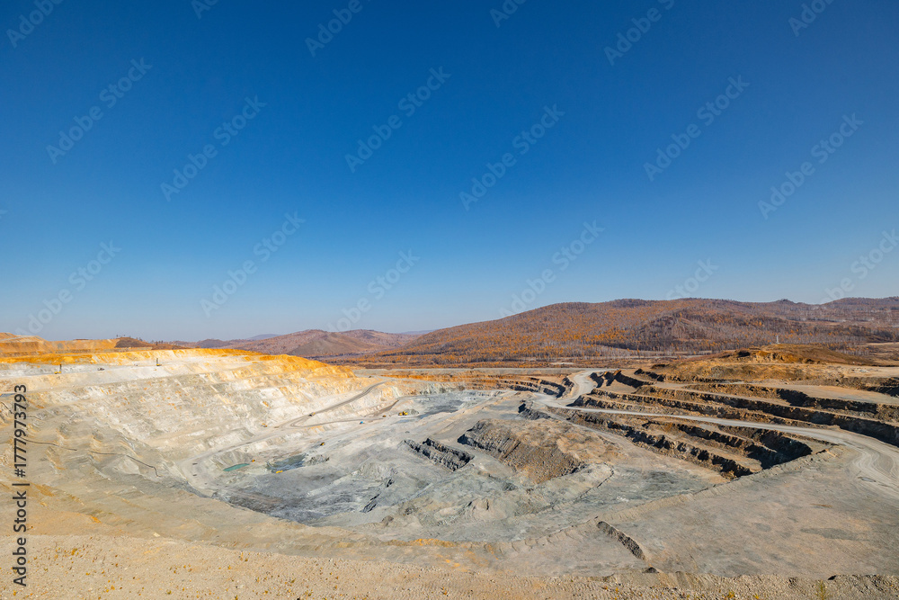 Obraz premium Panorama of open pit mine extracting gold, iron ore with heavy trucks, excavators.