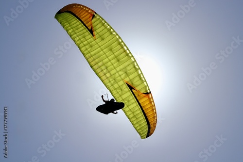 Papier peint A paraglider soars beneath a bright sky, framed against the sun.